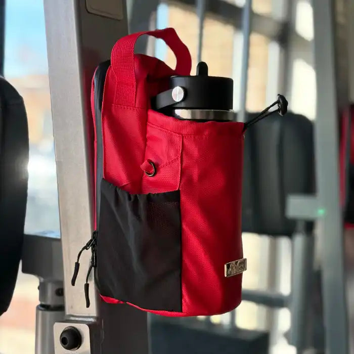 Red Nimbis magnetic gym bag attached to a metal gym rack, holding a water bottle with a blurred gym background.