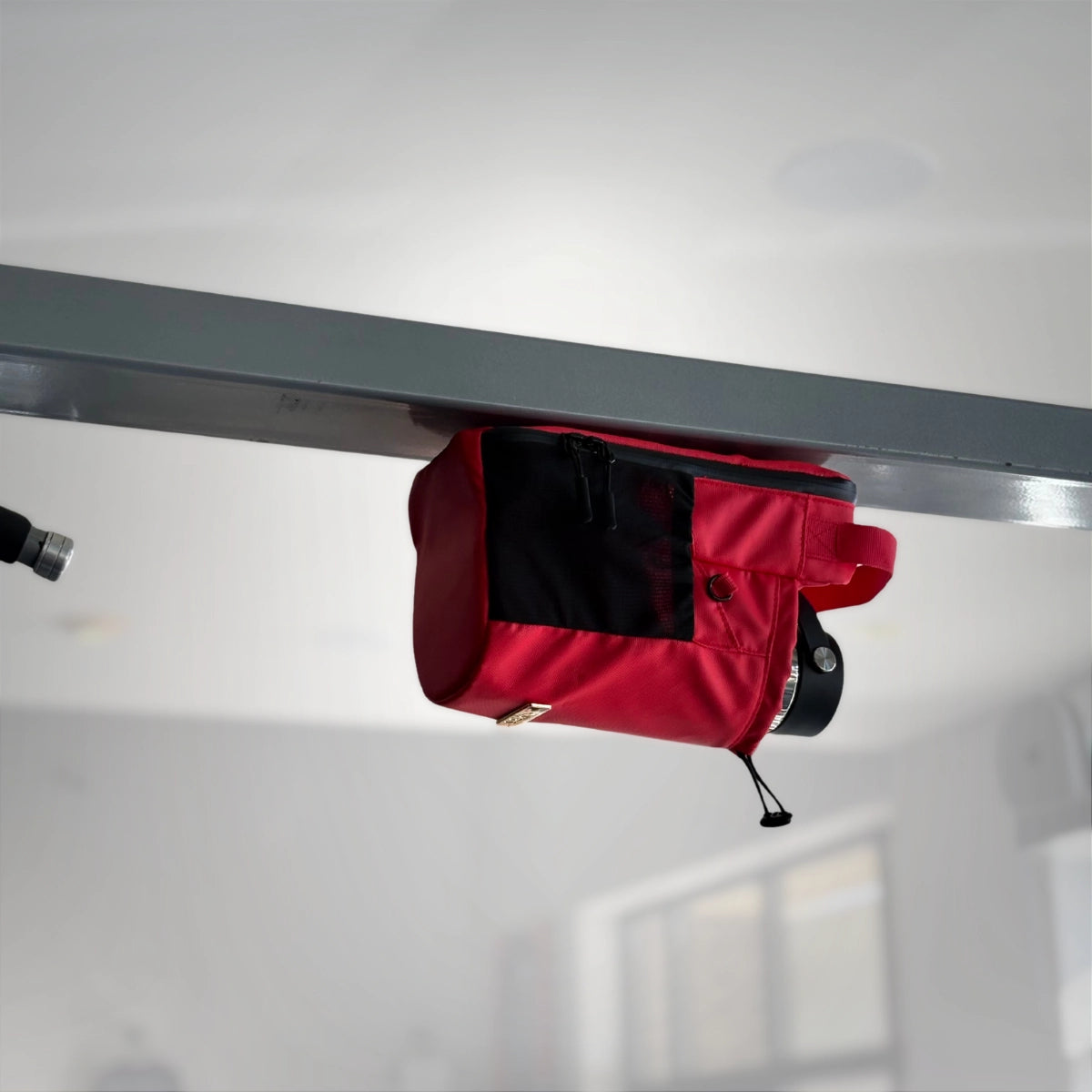 Red Nimbis magnetic gym bag securely hanging upside down from a metal beam, showing the strength of the built-in magnets.
